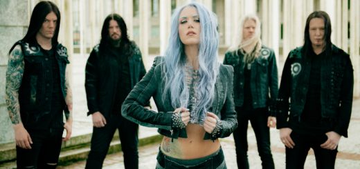 Die Band Arch Enemy im Gruppenbild. Sängerin Alissa steht vorne mittig und ist scharf gestellt. Die übrigen Bandmitglieder stehen etwas weiter hinten im unscharfen Hintergrund.