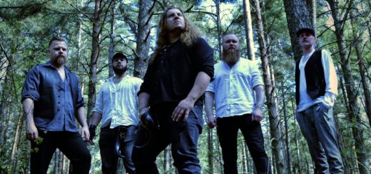 Die fünf Musiker stehen als Gruppe im Wald und kucken in verschiedene Richtungen. Sie haben weiße und dunkle Hemden, fallweise mit Westen, an.