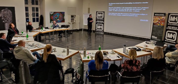 Menschen, Marken, Moshpits: Blick auf das im Halbkreis sitzende Publikum. Ein Referent blickt auf seine Präsentation.