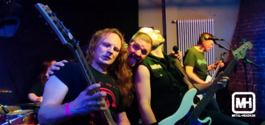 Der Sänger von Ignition streckt die Zunge heraus, während er zwischen Gitarrist und Bassist den Kopf herausstreckt.