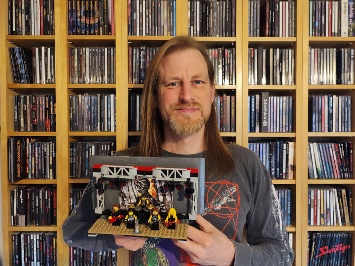 Jan mit einer Lego-Bühne in der Hand vor seinen CD-Regalen stehend