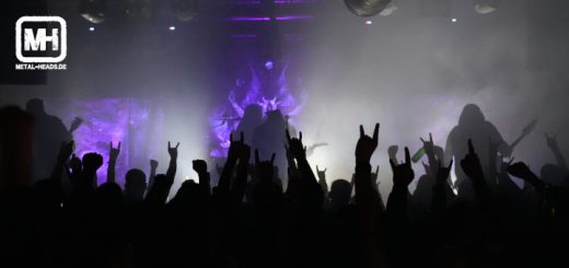 UADA live in Dortmund 2023: UADA auf der Bühne in blauem Licht. Im dunklen Vordergrund jede Menge Fans mit gehörnten Händen.