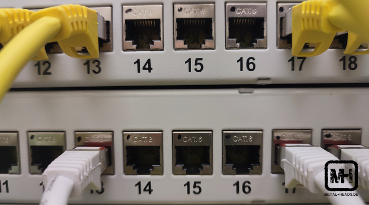 Nahaufnahme auf eine Vielzahl von Netzwerk-Steckplätzen, teilweise mit gelben und weißen Kabeln besetzt. Die einzelnen Steckplätze sind mit Ziffern beschriftet.
