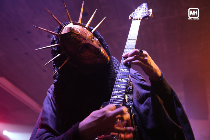 Der Sänger und Gitarrist von Imperial Triumphant hält sein Instrument senkrecht, hält den Kopf schräg und blickt in die Kamera.