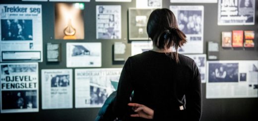 Blick auf Zeitungsartikel an der Wand. Davor steht eine junge Frau und blickt auf die gezeigten Presseartikel.