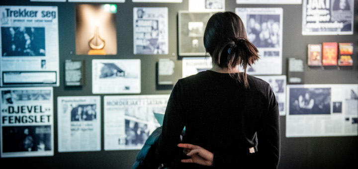 Blick auf Zeitungsartikel an der Wand. Davor steht eine junge Frau und blickt auf die gezeigten Presseartikel.