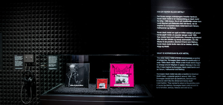 Blick auf eine Wand in der Ausstellung mit Platten von Darkthrone und Mayhem. Rechts erklärender Text und linke ein Kopfhörer.