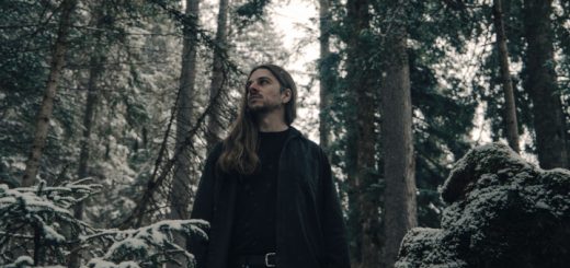 Vinsta: Der Musiker in schwarzer Kleidung blickt in die Ferne, während er im verschneiten Wald steht.