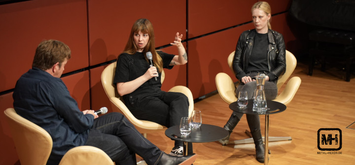 Podiumsdiskussion mit Sara Gacic in der Mitte und Linnea Olson rechts. Journalist Andreas Krieger hört aufmerksam zu, während Sara Gacic vehement spricht und gestikuliert.