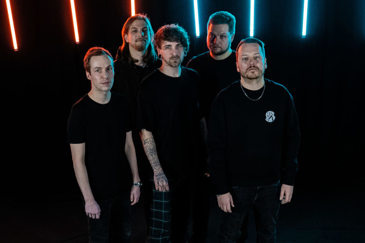 Die Band Aftermath steht schwarz gekleidet im Dunklen vor bunten Neonröhren.