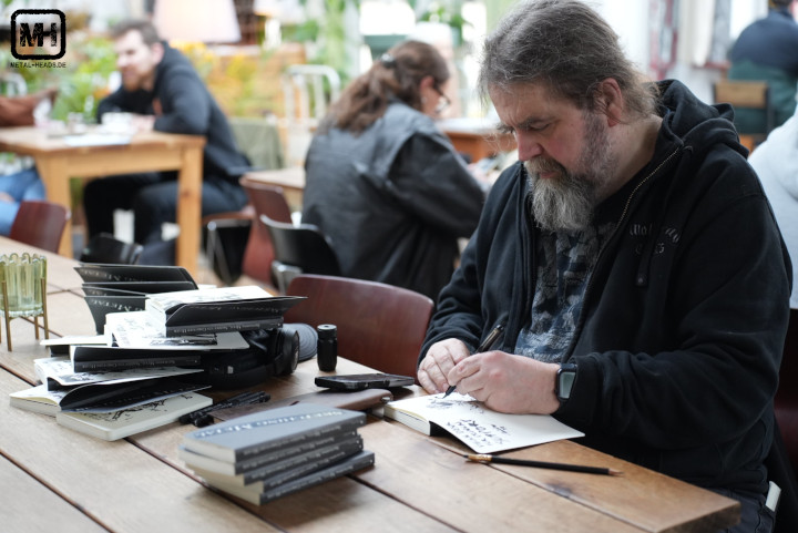 Christoph Heuer signiert Bücher. Auf dem Tisch liegen stapelweise Bücher mit individuellen Skizzen.