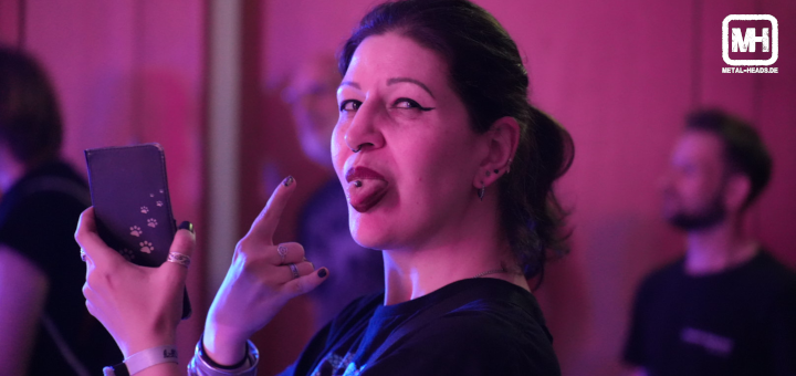 Luna, die Veranstalterin des Azadi Festival 2024, streckt die Zunge mit Piercing heraus und zeigt die gehörnte Hand, während die linke Hand ihr Smartphone hält, mit dem sie die Veranstaltung filmt.
