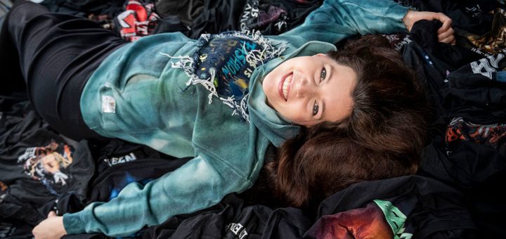 Alex Weber von Alextravagant liegt auf einem Berg alter Tour- und Festivalshirts.