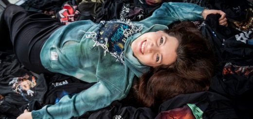 Alex Weber von Alextravagant liegt auf einem Berg alter Tour- und Festivalshirts.