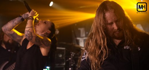 HIRAES live im Pitcher Düsseldorf, 27.06.2024: Vorne rechts im Bild Gitarrist Lukas, der sich konzentriert. Rechts hinten im Bild Sängerin Britta, die das Mikro mit beiden Händen hält und hineinschreit, während sie den Kopf in den Nacken wirft.