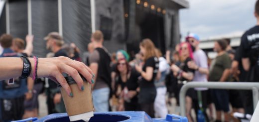 Eine Frauenhand mit lackierten Fingernägeln wirft einen Einweg-Kaffeebecher in eine Mülltonne