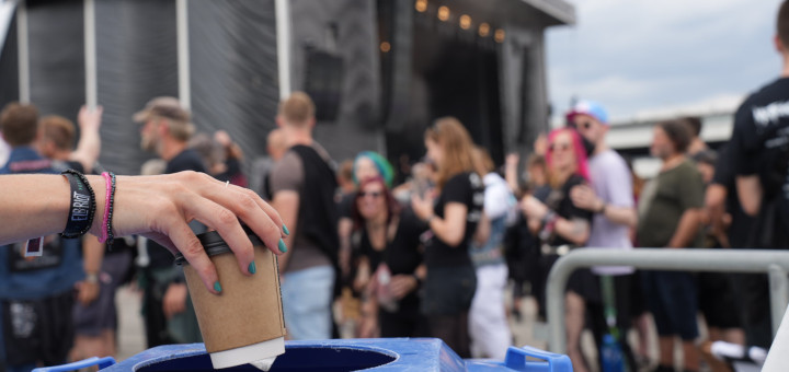 Eine Frauenhand mit lackierten Fingernägeln wirft einen Einweg-Kaffeebecher in eine Mülltonne