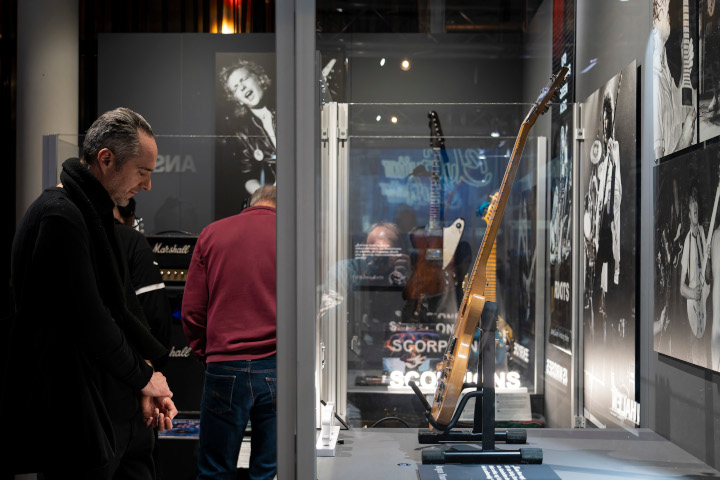 Ein Mensch steht andächtig vor einer ausgestellten Gitarre. Der Blick ist rechtwinklig auf das Szenario.