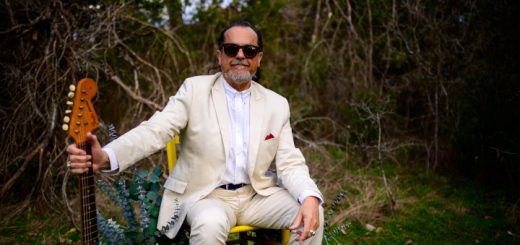 Tito Larriva sitzt im Garten auf einem gelben Stuhl und hält die Gitarre neben sich.