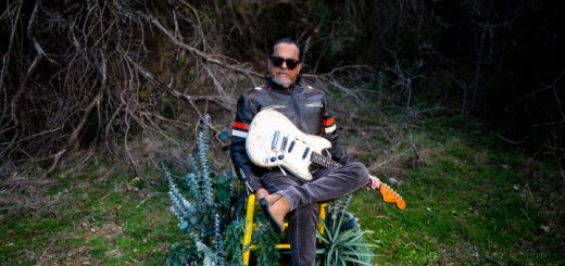 Tito Larriva sitzt im Garten auf einem gelben Stuhl und hält die Gitarre auf dem Schoss.