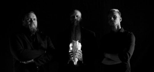 Bandfoto von SERPENT GOD, alles fast in schwarz, man sieht nur leicht die hellen Gesichter. Der Mensch in der Mitte hält einen weißen Tierschädel in den Händen.