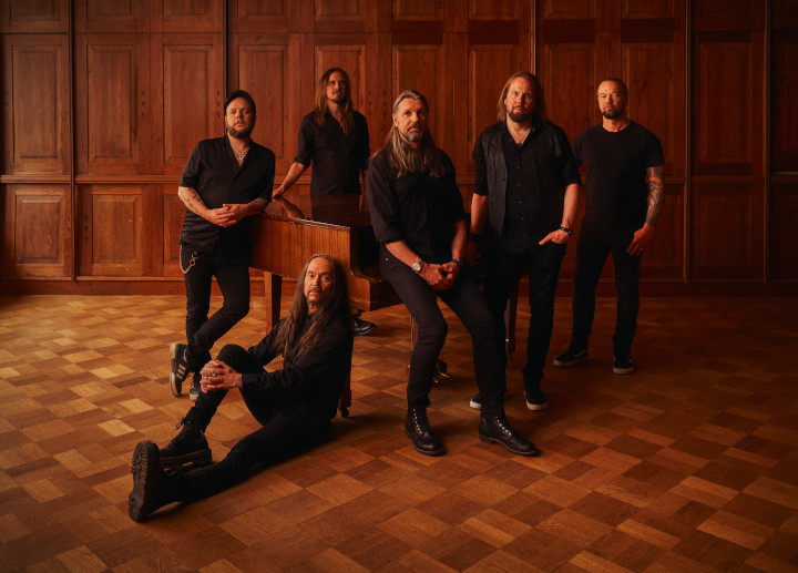 Amorphis stehen in einem alten Musikzimmer um einen Flügel oder ähnliches herum. Eine Person sitzt und lehnt am Instrument.