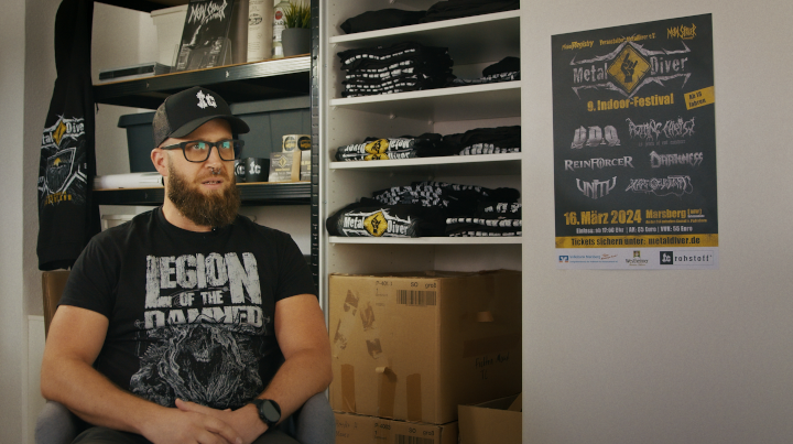 Ein Mensch in einer Interviewsituation, im Hintergrund Festivalmerch.