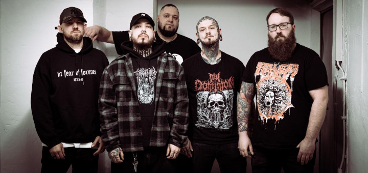 Die fünf Bandmitglieder stehen vor weißen Kellerwänden.