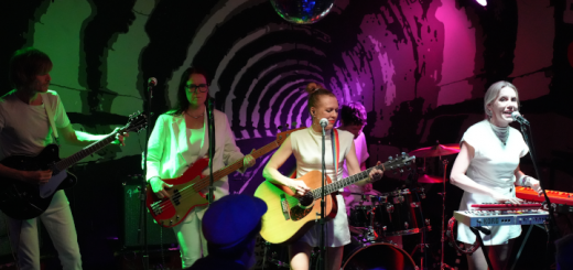 Blick auf die Bühne mit allen Mitgliedern von Hellsongs; im Vordergrund erahnt man das Publikum.