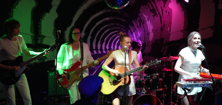 Blick auf die Bühne mit allen Mitgliedern von Hellsongs; im Vordergrund erahnt man das Publikum.