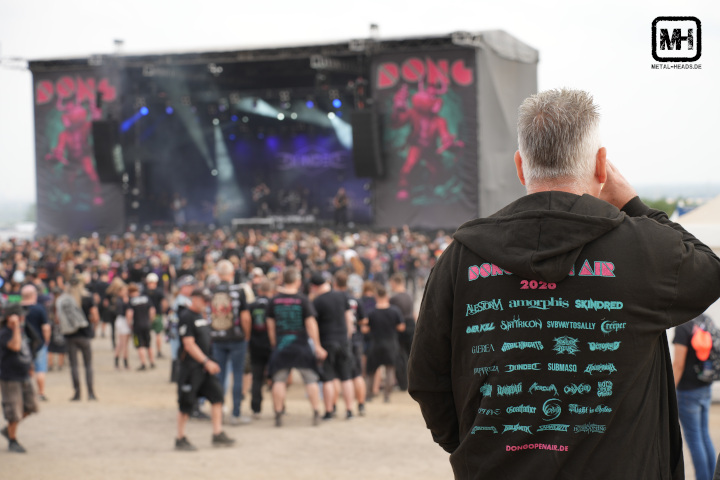 Ein Mensch trägt ein Festivalhoody des Dong 2026, im Hintergrund ist unscharf die Bühne zu sehen.