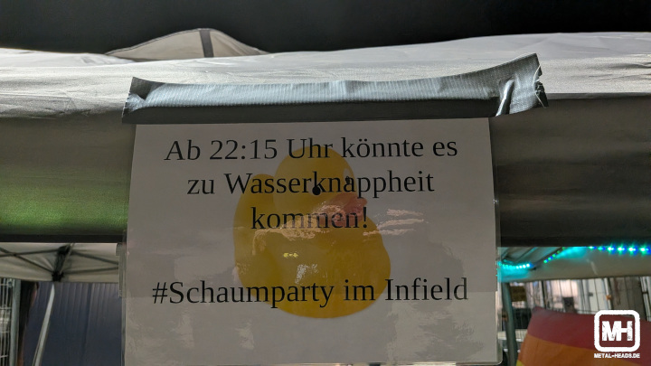Infoschild mit Aufschrift: "Ab 22:15 Uhr könnte es zu Wasserknappheit kommen! #Schaumparty im Infield".